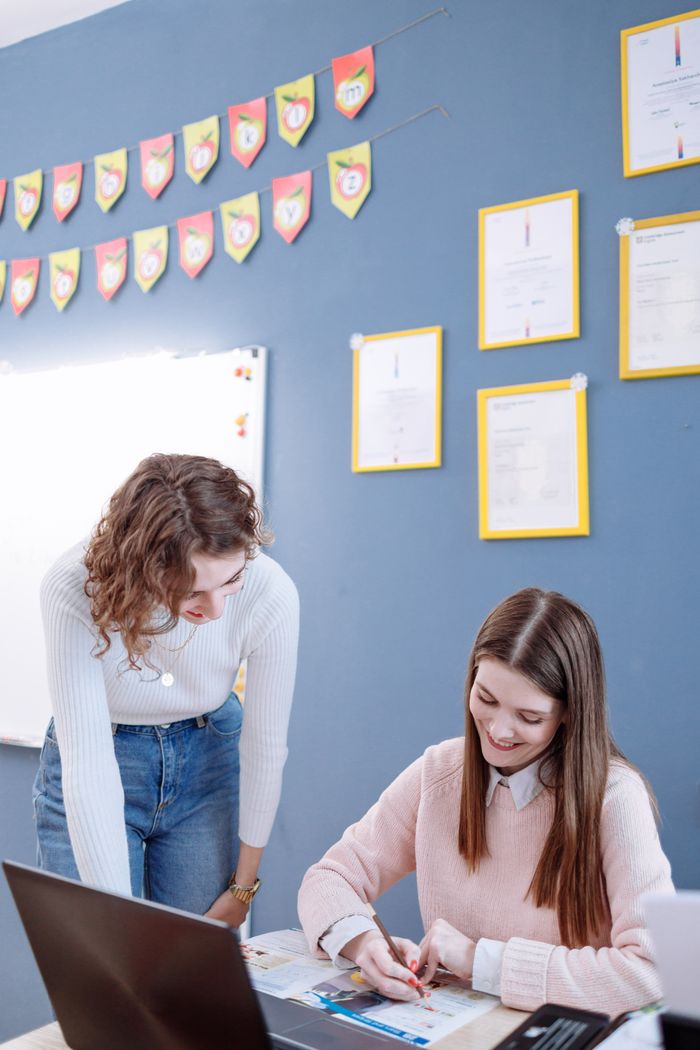 Crafting Captivating Headlines: Your awesome post title goes here Young woman helping a student with assignments in a classroom setting, fostering learning.